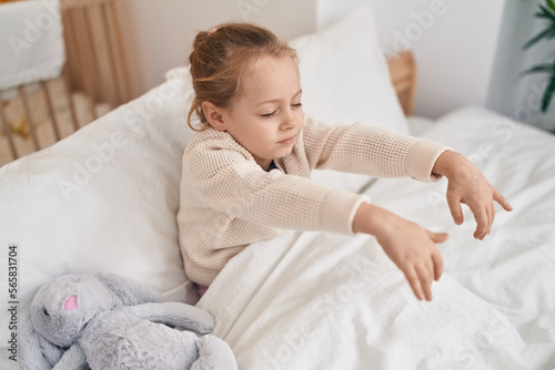 Adorable blonde girl somnambulist sitting on bed at bedroom photo