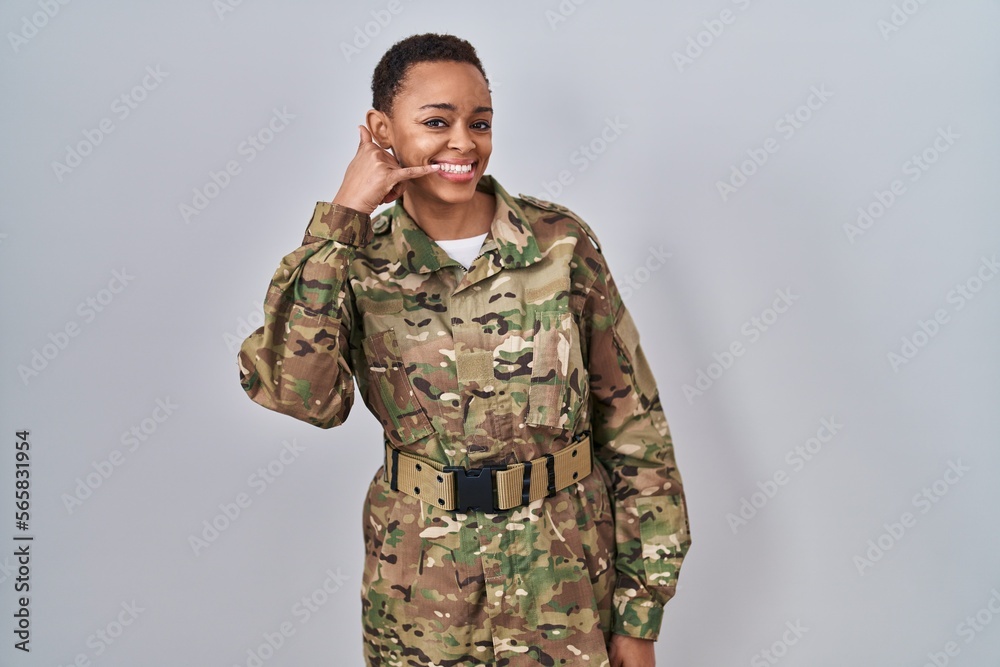 Beautiful african american woman wearing camouflage army uniform smiling doing phone gesture with hand and fingers like talking on the telephone. communicating concepts.