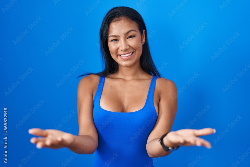 Hispanic woman standing over blue background smiling cheerful offering hands giving assistance and acceptance. Hispanic woman standing over blue background smiling cheerful offering hands giving assistance and acceptance.