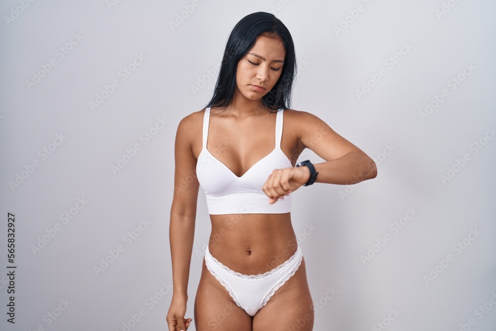 Fototapeta premium Hispanic woman wearing lingerie checking the time on wrist watch, relaxed and confident