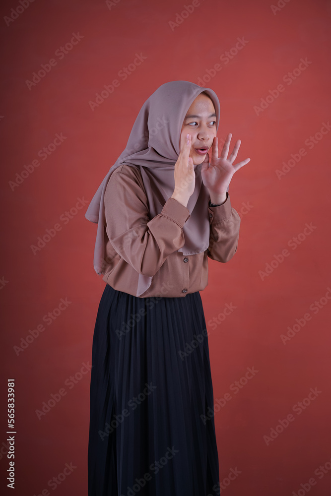 Beautiful Asian woman in brown shirt and hijab smiling cheerfully whispering over brown background