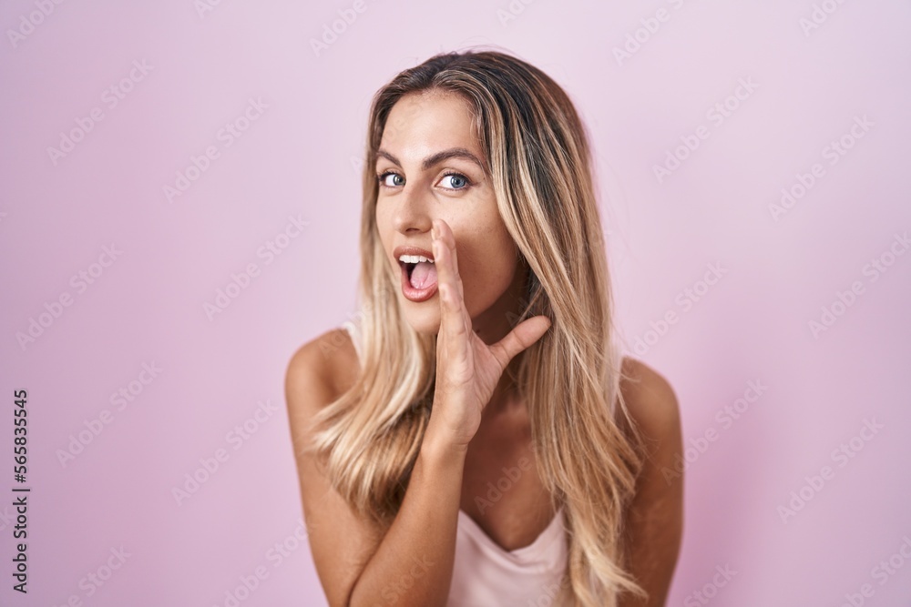 Young blonde woman standing over pink background hand on mouth telling secret rumor, whispering malicious talk conversation Young blonde woman standing over pink background hand on mouth telling secret rumor, whispering malicious talk conversation