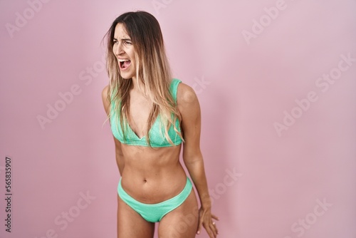 Young hispanic woman wearing bikini over pink background angry and mad screaming frustrated and furious, shouting with anger. rage and aggressive concept.