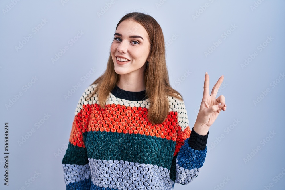 Young hispanic girl standing over blue background smiling looking to the camera showing fingers doing victory sign. number two. Young hispanic girl standing over blue background smiling looking to the camera showing fingers doing victory sign. number two.