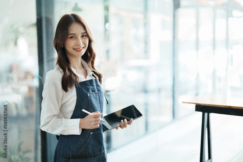 Fototapeta premium open a small business Portrait of happy Asian woman in apron holding tablet in front of cafe.