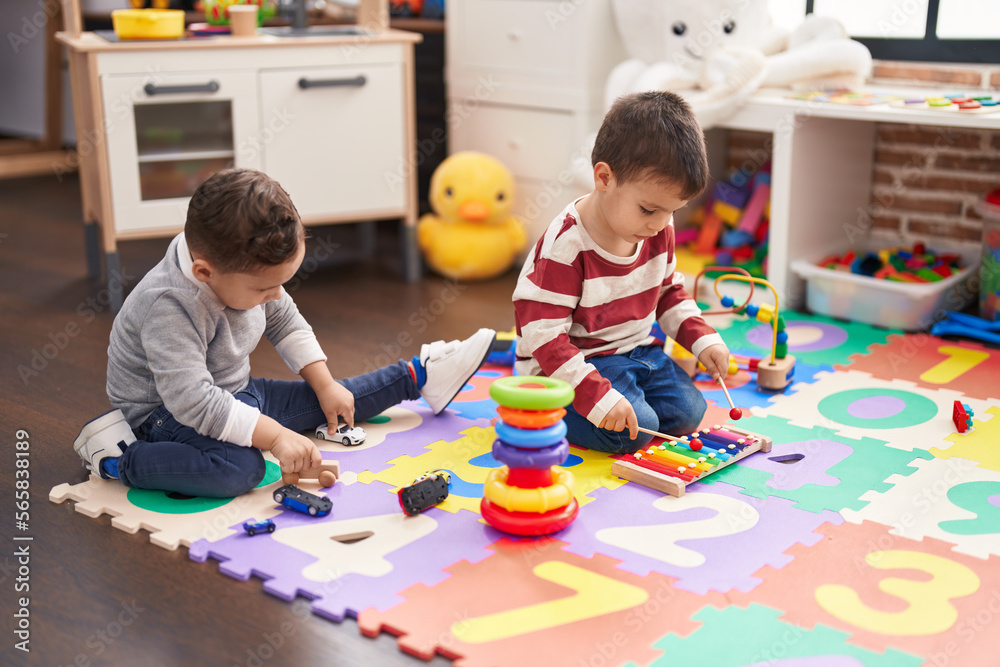 Fototapeta premium Two kids playing xylophone holding car toy sitting on floor at kindergarten