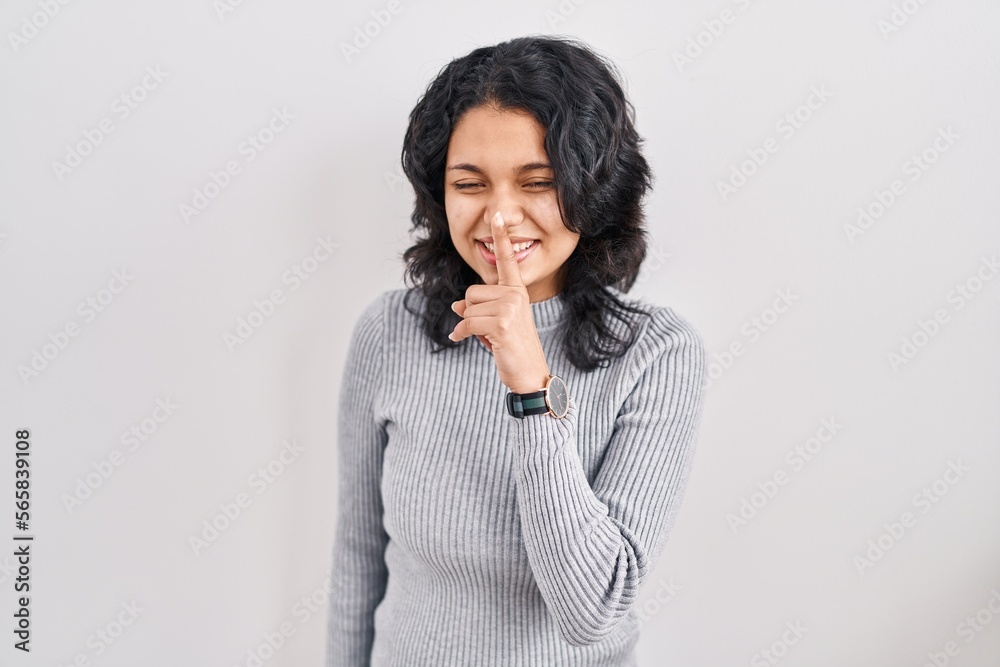 Hispanic woman with dark hair standing over isolated background asking to be quiet with finger on lips. silence and secret concept. Hispanic woman with dark hair standing over isolated background asking to be quiet with finger on lips. silence and secret concept.