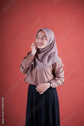 Beautiful Asian woman in brown shirt and hijab smiling cheerfully hand on chin on brown background