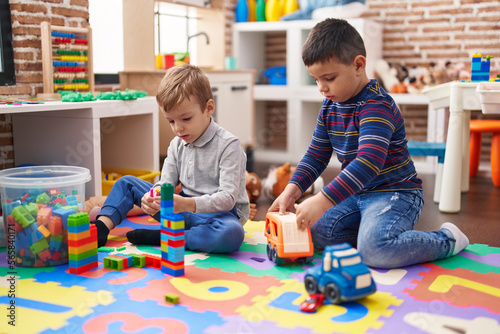 Two kids playing with construction blocks and truck toy sitting on floor at kindergarten