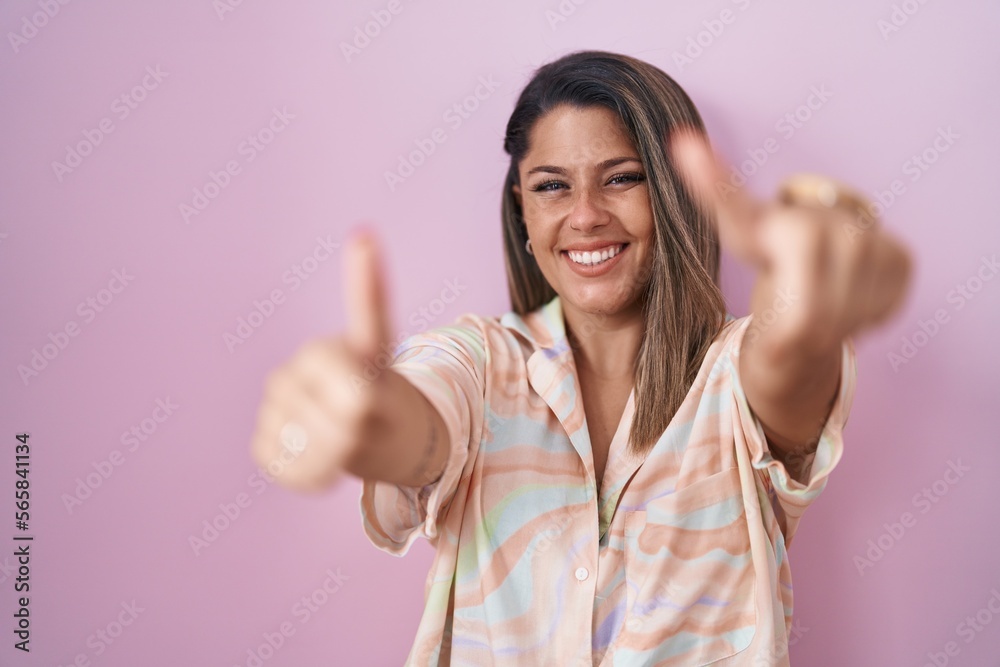 Blonde woman standing over pink background approving doing positive gesture with hand, thumbs up smiling and happy for success. winner gesture. Blonde woman standing over pink background approving doing positive gesture with hand, thumbs up smiling and happy for success. winner gesture.