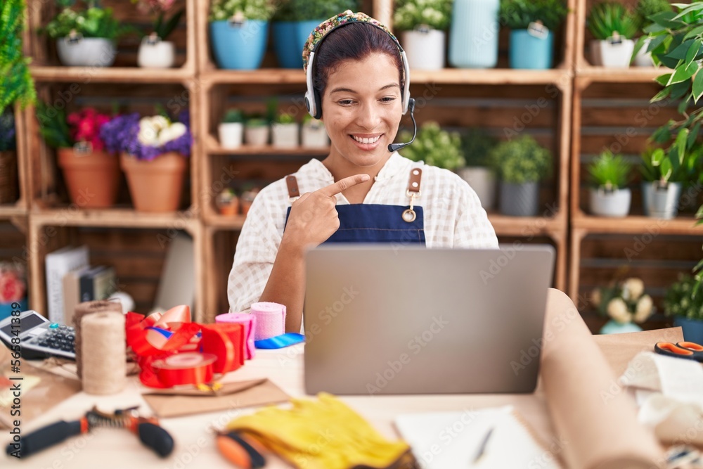 Young hispanic woman working at florist shop doing video call smiling happy pointing with hand and finger Young hispanic woman working at florist shop doing video call smiling happy pointing with hand and finger