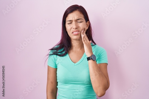 Young hispanic woman standing over pink background touching mouth with hand with painful expression because of toothache or dental illness on teeth. dentist