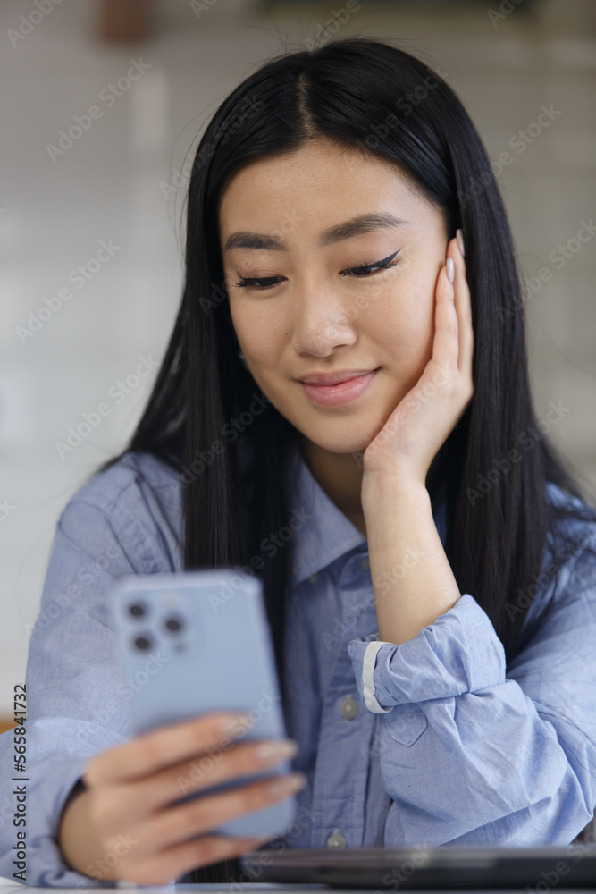 Beautiful POC girl from southeast asia browsing mobile app on smart phone. Portrait of young asian woman using modern blue mobile phone Beautiful POC girl from southeast asia browsing mobile app on smart phone. Portrait of young asian woman using modern blue mobile phone
