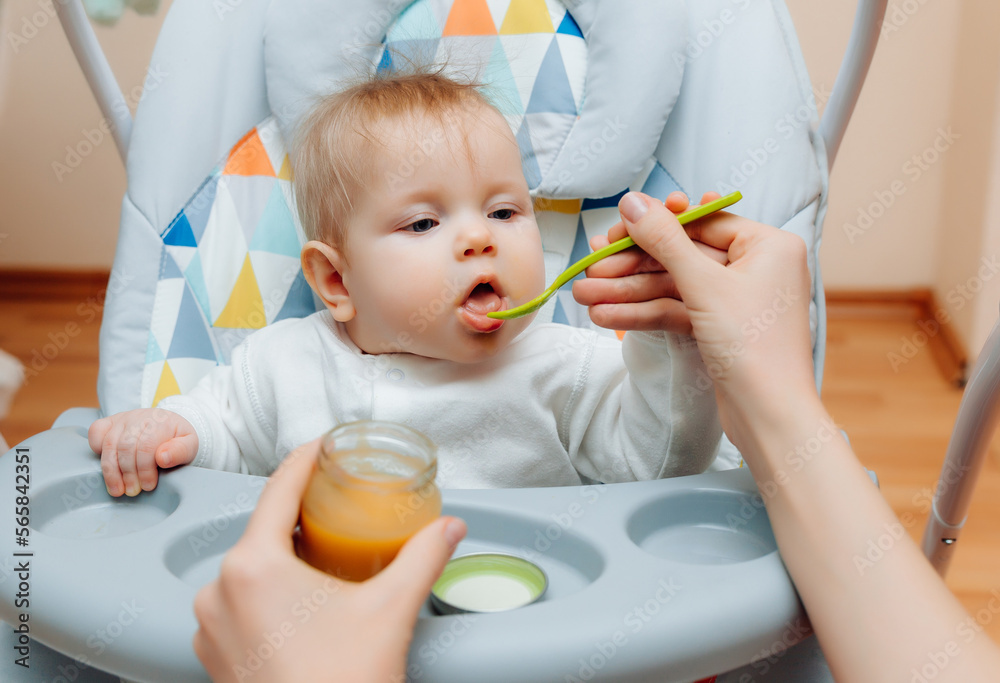 Mother gives fruit sauce to baby.mom feeds baby on highchair.baby food Mother gives fruit sauce to baby.mom feeds baby on highchair.baby food