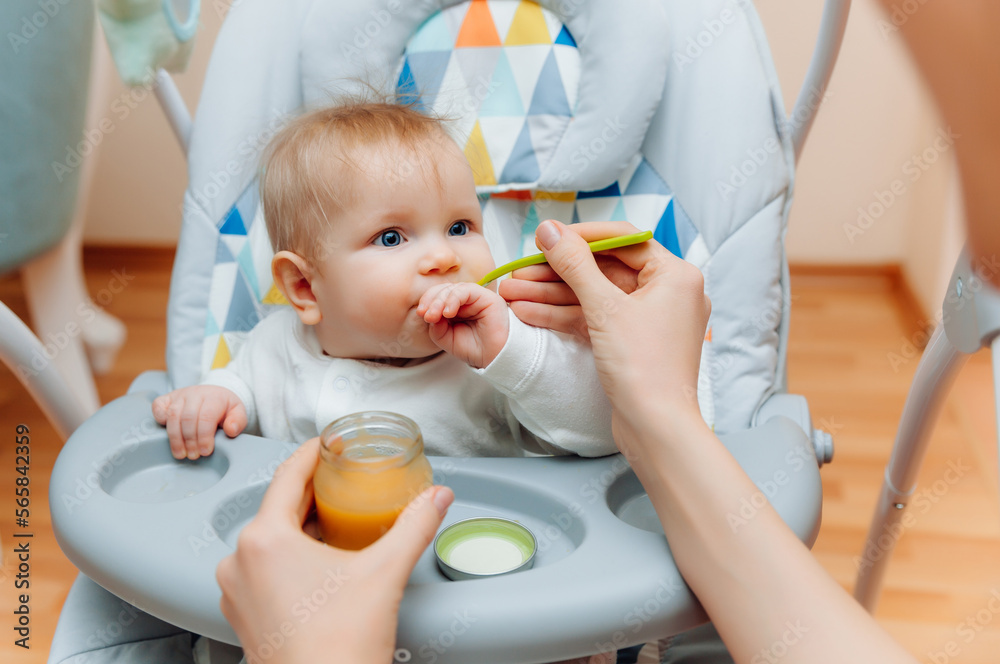Mother gives fruit sauce to baby.mom feeds baby on highchair.baby food Mother gives fruit sauce to baby.mom feeds baby on highchair.baby food