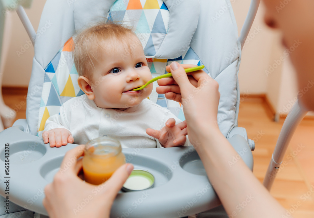 Mother gives fruit sauce to baby.mom feeds baby on highchair.baby food Mother gives fruit sauce to baby.mom feeds baby on highchair.baby food