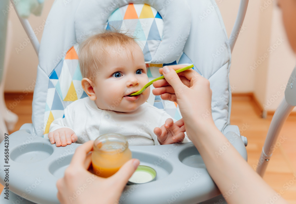 Mother gives fruit sauce to baby.mom feeds baby on highchair.baby food Mother gives fruit sauce to baby.mom feeds baby on highchair.baby food