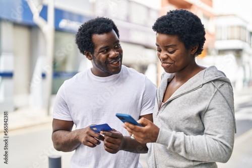 African american man and woman couple using smartphone and credit card at street