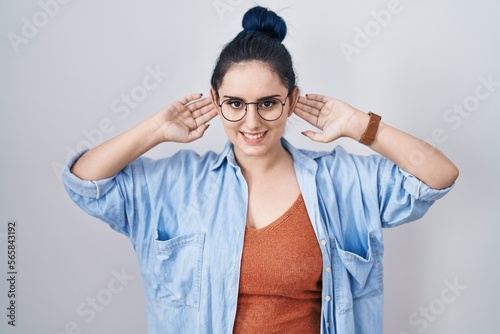 Young modern girl with blue hair standing over white background smiling pulling ears with fingers  funny gesture. audition problem