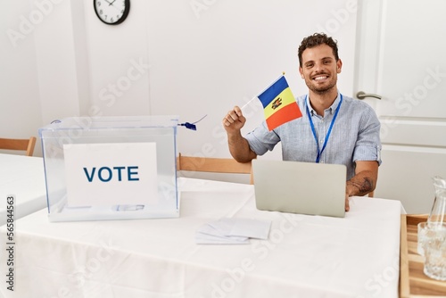 Young hispanic man smiling confident holding moldova flag working at electoral college
