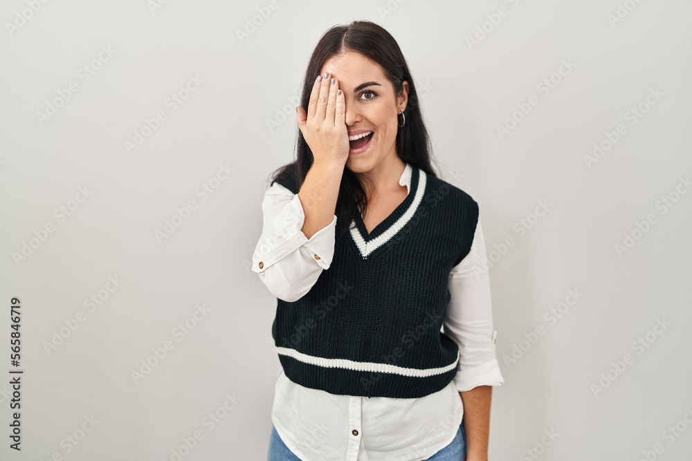 Young hispanic woman standing over isolated background covering one eye with hand, confident smile on face and surprise emotion. Young hispanic woman standing over isolated background covering one eye with hand, confident smile on face and surprise emotion.