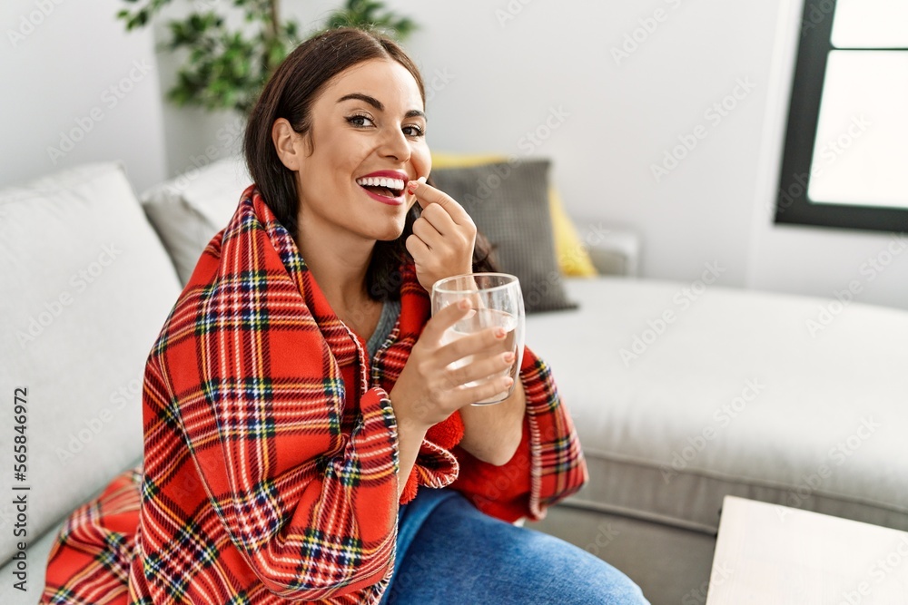 Young beautiful hispanic woman taking pill sitting on sofa at home Young beautiful hispanic woman taking pill sitting on sofa at home