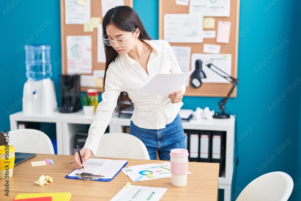 Young chinese woman business worker reading document writing on paperwork at office Young chinese woman business worker reading document writing on paperwork at office