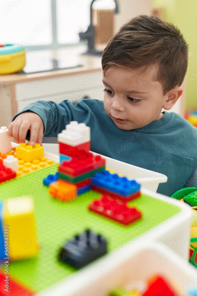 Adorable hispanic boy playing with construction blocks sitting on table at kindergarten
