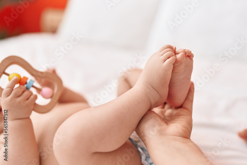 Adorable hispanic toddler lying on bed having feet massage at bedroom