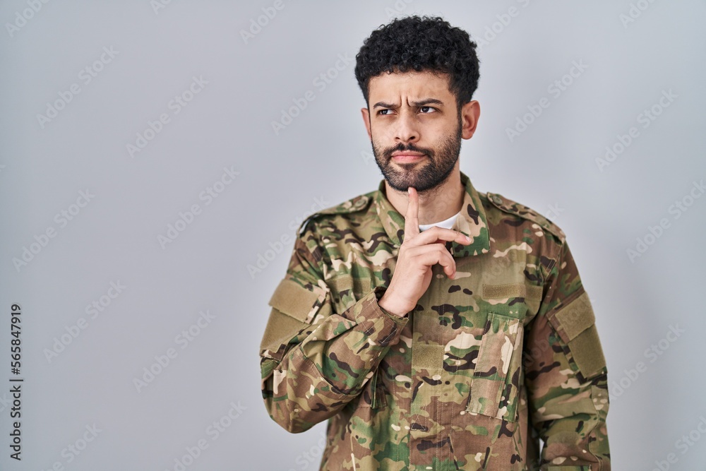 Arab man wearing camouflage army uniform thinking concentrated about doubt with finger on chin and looking up wondering