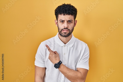 Arab man standing over yellow background pointing aside worried and nervous with forefinger, concerned and surprised expression