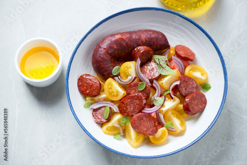 Plate of salad with yellow tomatoes, warm chorizo and red onion, horizontal shot on a grey granite background, elevated view