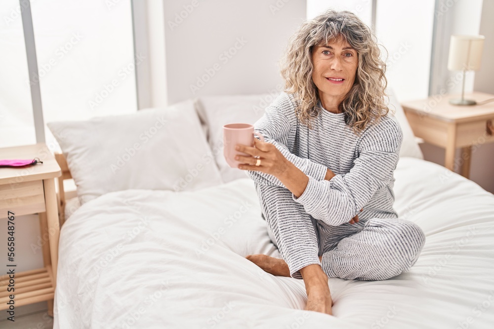 Middle age woman drinking cup of coffee sitting on bed at bedroom Middle age woman drinking cup of coffee sitting on bed at bedroom
