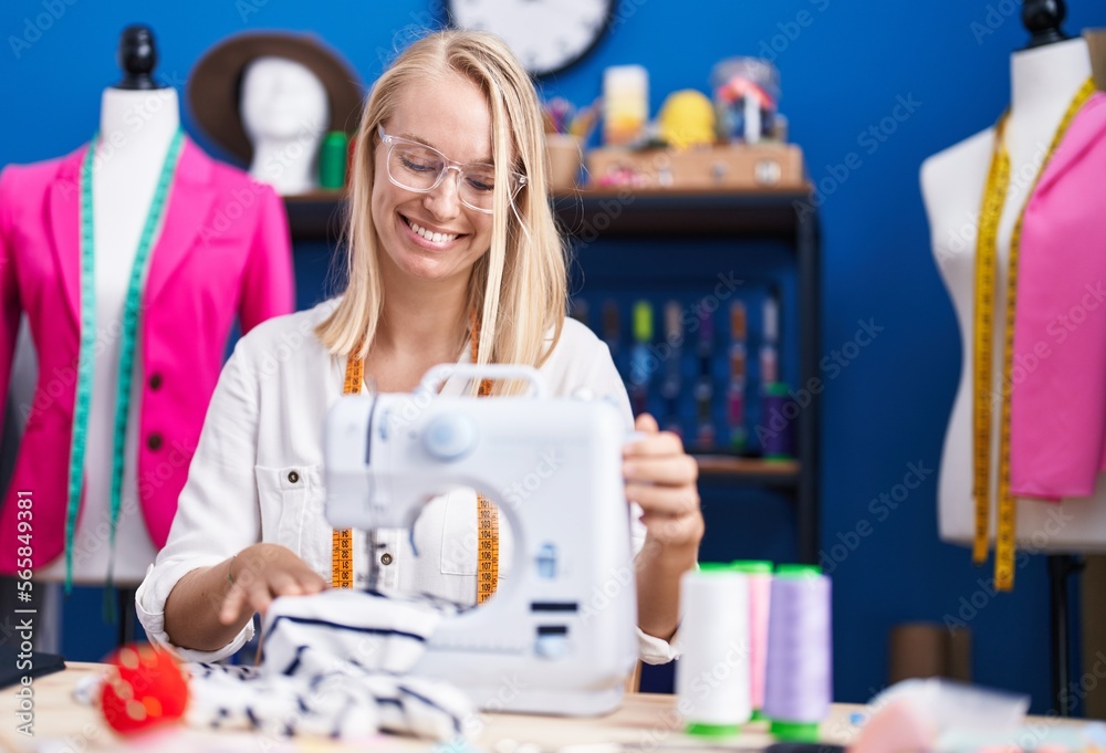 Young blonde woman tailor smiling confident using sewing machine at sewing studio
