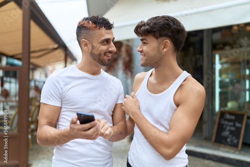 Two hispanic men couple smiling confident using smartphone at coffee shop terrace