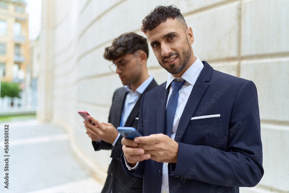 Fototapeta premium Two hispanic men business workers smiling confident using smartphones at street
