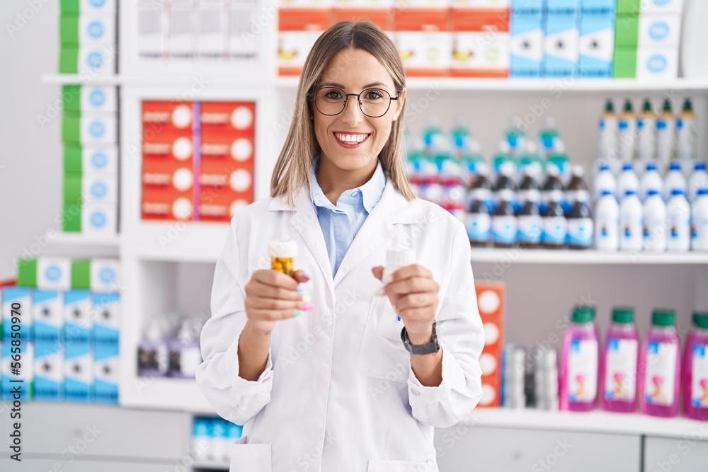 Young beautiful hispanic woman pharmacist smiling confident holding pills bottles at pharmacy