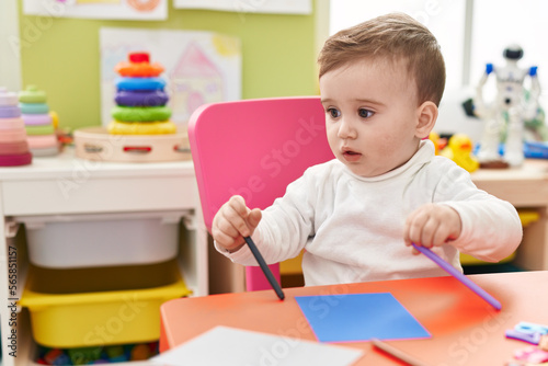 Adorable caucasian baby student sitting on table drawing on paper at kindergarten