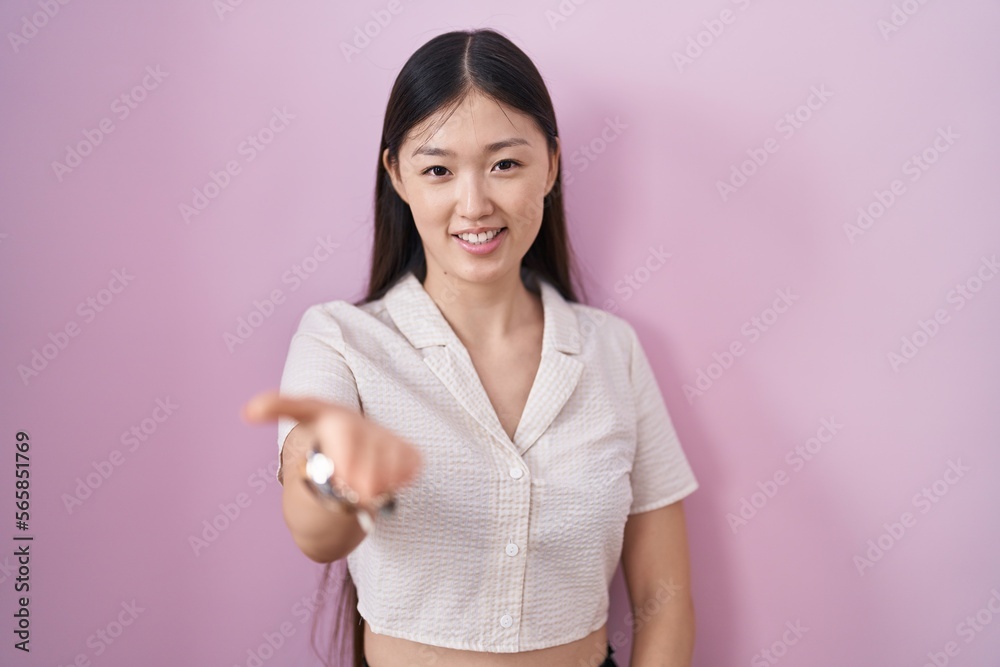 Chinese young woman standing over pink background smiling cheerful offering palm hand giving assistance and acceptance.