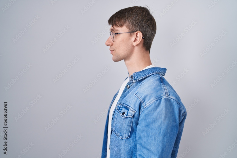 Caucasian blond man standing wearing glasses looking to side, relax profile pose with natural face and confident smile.