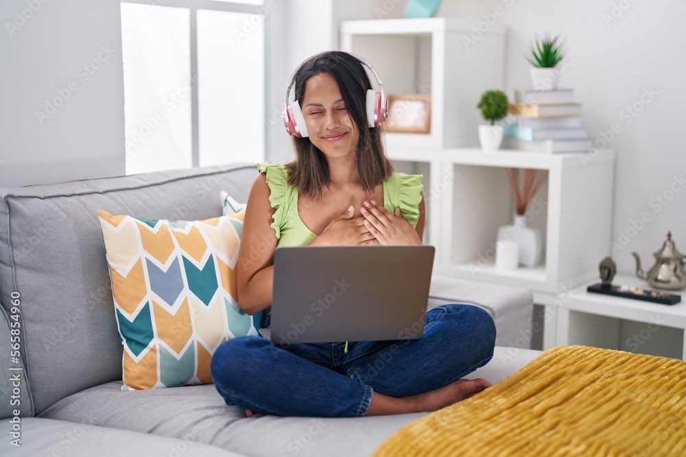 Hispanic young woman using laptop at home smiling with hands on chest with closed eyes and grateful gesture on face. health concept. Hispanic young woman using laptop at home smiling with hands on chest with closed eyes and grateful gesture on face. health concept.