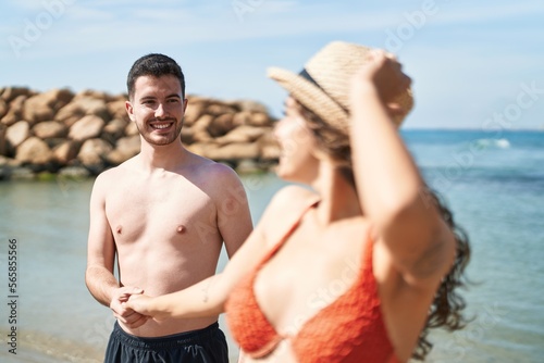 Young hispanic couple tourists wearing swimsuit standing with hands together at seaside