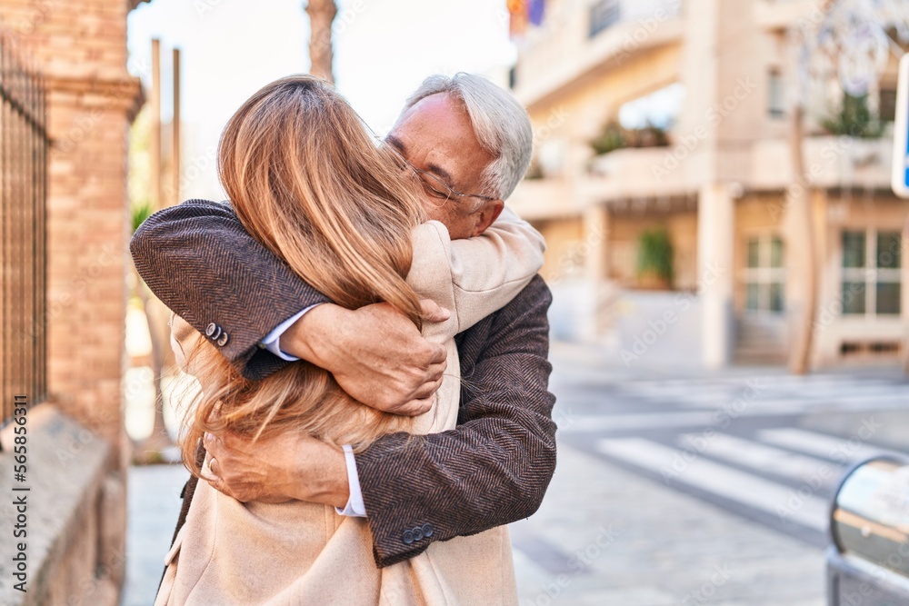 Naklejka premium Middle age man and woman couple hugging each other standing at street