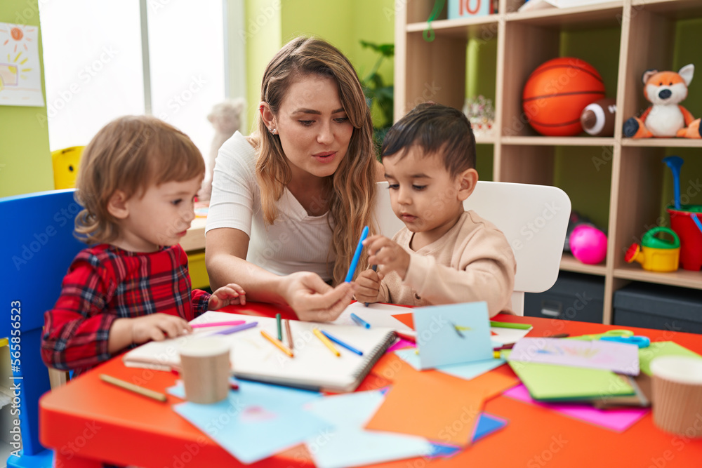 Teacher with boys sitting on table drawing on paper at kindergarten Teacher with boys sitting on table drawing on paper at kindergarten