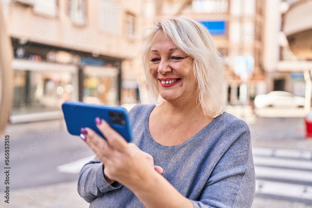 Middle age blonde woman smiling confident using smartphone at street