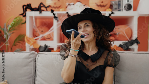 Middle age hispanic woman sending voice message by smartphone having halloween party at home