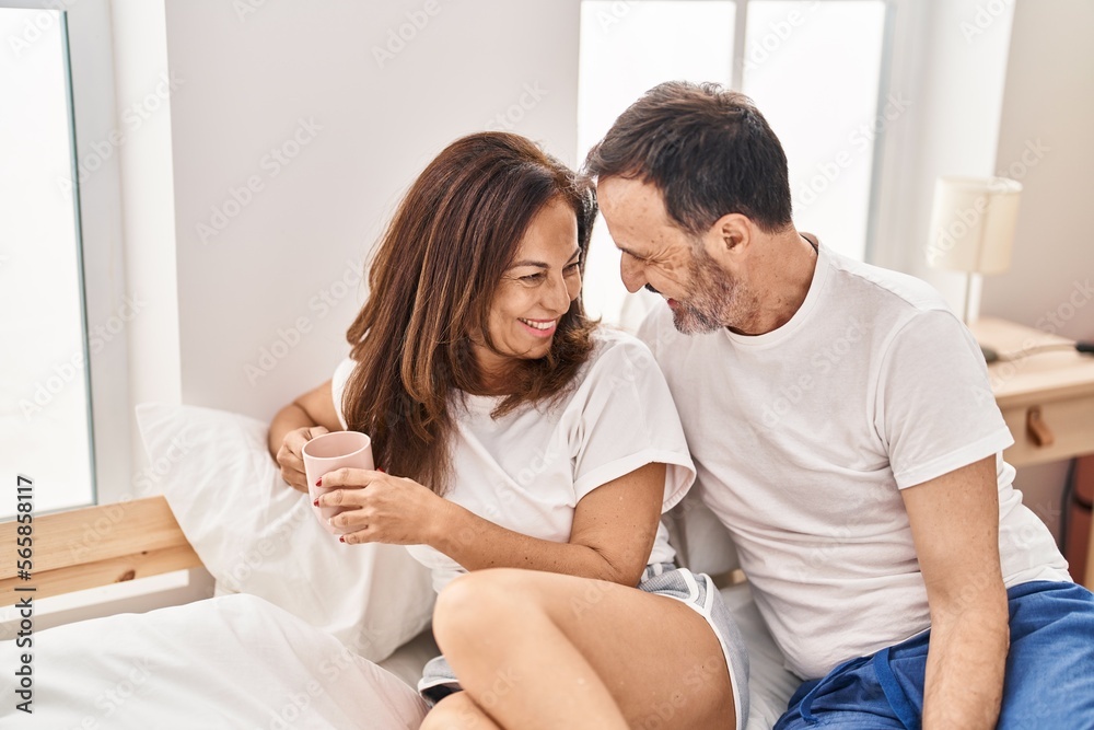 Middle age man and woman couple drinking coffee sitting on bed at bedroom Middle age man and woman couple drinking coffee sitting on bed at bedroom