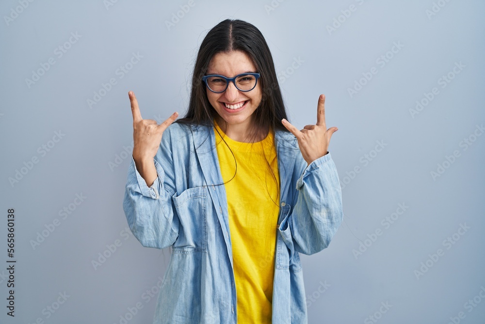 Young hispanic woman standing over blue background shouting with crazy expression doing rock symbol with hands up. music star. heavy music concept. Young hispanic woman standing over blue background shouting with crazy expression doing rock symbol with hands up. music star. heavy music concept.
