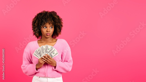 Pensive cheerful young african american curly female in casual holds a lot of money cash and looks at empty space