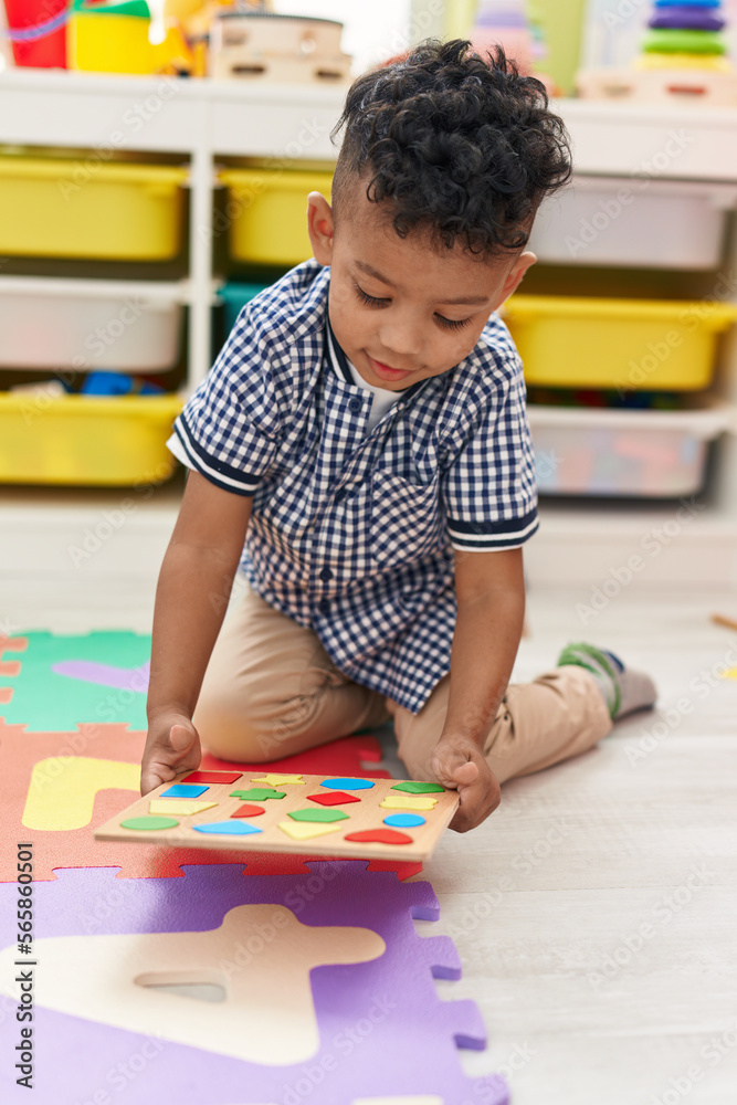 African american boy playing with maths puzzle game sitting on floor at kindergarten African american boy playing with maths puzzle game sitting on floor at kindergarten